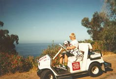 a man riding on the back of a white golf cart down a dirt road next to the ocean