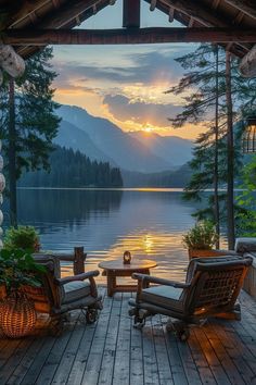 two chairs sitting on top of a wooden deck next to a lake with mountains in the background