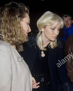 two women standing next to each other in front of a man with long blonde hair