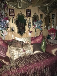 a bed covered in lots of pillows next to a wall with pictures and mirrors on it