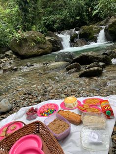 a picnic table with food and drinks on it next to a stream in the woods