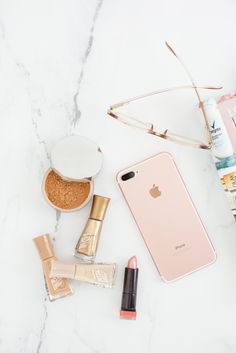 an iphone, lipstick, and other cosmetics on a marble counter top with the contents laid out