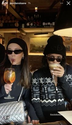 three women sitting at a table with drinks in their hands and one holding a purse