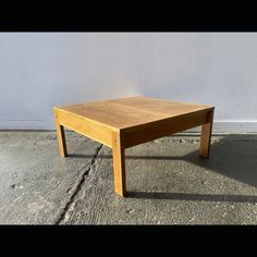 a square wooden table sitting on top of cement floor next to a white brick wall