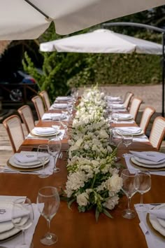 a long table set with white flowers and place settings for an outdoor dinner party in the garden