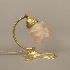 an antique brass table lamp with a pink glass shade on the base and a gold plated metal arm