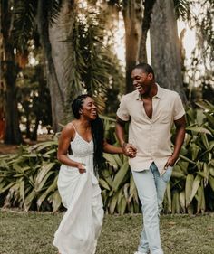 a man and woman holding hands walking through the grass with palm trees in the background