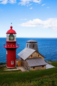 a red and white light house sitting on top of a lush green field next to the ocean