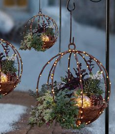 three hanging planters filled with plants and lit up lights in the middle of snow