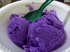 two scoops of purple ice cream in a white paper bowl with green plastic spoon