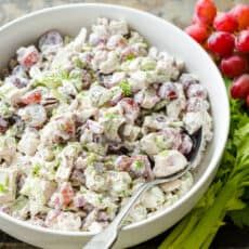 a white bowl filled with salad next to grapes and celery on a table