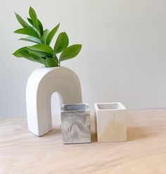 a white vase with a plant in it next to two smaller square containers on a table