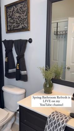 a white toilet sitting next to a bathroom sink under a large mirror with black towels hanging on it