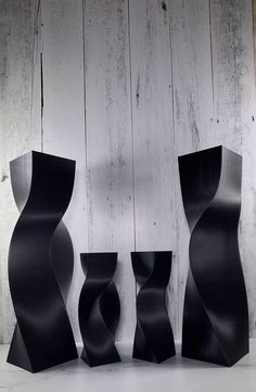 three black vases sitting next to each other on a white surface with wood paneling behind them