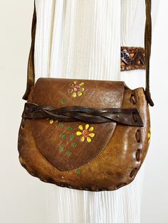 |d e s c r i p t i o n| *circa 1970s *beautiful hippie leather purse from the 70s, came from original owner  *hand tooled design with painted yellow daisies  *saddle flap in front with strap  *a good length arm strap, could be snug cross body purse  *clean inside, well taken care of!  *authentic boho/hippie shoulder bag  |i n f o| tag: none  condition: very good! A few stretches on outside of leather.  |m e a s u r e m e n t s| total length with strap: 22" length of purse: 8.5" height of purse: Retro Hand-tooled Bags, Hippie Brown Leather Bag, Mid-century Leather Shoulder Bag For Daily Use, Mid-century Leather Shoulder Bag, Mid-century Brown Leather Bags, Brown Retro Shoulder Bag With Hand Tooled Details, Handmade Vintage Brown Shoulder Bag, Retro Vintage Brown Hand Tooled Shoulder Bag, Hippie Leather Bag For Festivals