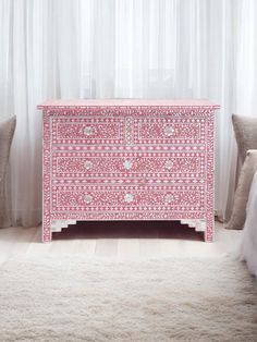 a pink chest of drawers sitting in front of a white curtained window next to two pillows