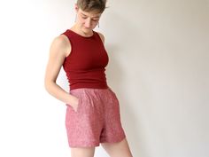 a woman standing in front of a white wall wearing red shorts and a tank top