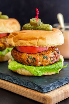 two burgers with lettuce, tomato and pickles on a cutting board