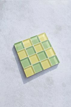 a yellow and green square shaped plate sitting on top of a cement floor next to a white wall