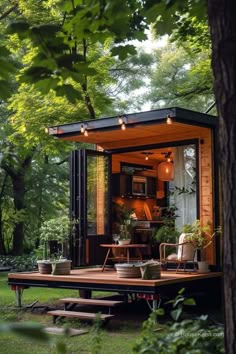 a tiny house in the woods surrounded by trees and greenery is lit up with lights