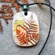 a necklace with a leaf design on it sitting on a table next to some leaves