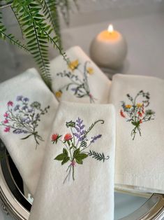 four embroidered napkins on a plate with a candle in the background