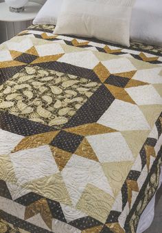 a bed with a quilt on top of it next to a night stand and lamp