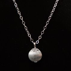 "This necklace has a chunky look to it without feeling heavy. The chain links are a large diamond shape and are flat, so they catch the light beautifully. The pendant is a brushed silver circle that looks a bit like a locket, but is closed. The pendant is held by nature-inspired bead caps on the top and bottom, which makes this a unique piece. The chain is 18\" long and the pendant is 1.25\" long. The necklace is fastened by a lobster clasp." Metal Circle, Silver Circle, Chain Links, Brushed Metal, Circle Pendant, Bead Caps, Diamond Shape, Nature Inspired, Diamond Shapes