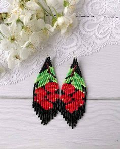 a pair of red and green beaded earrings next to white flowers on a table