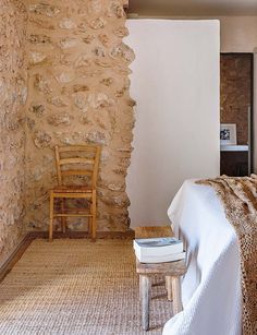 a bed sitting next to a wooden chair in a room with stone walls and flooring