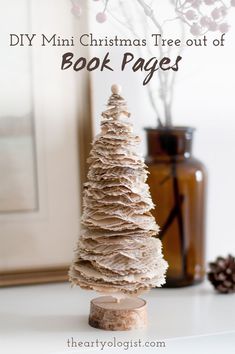 A little Christmas tree decoration made out of old book pages, sitting on a shelf with a vase of branches in the background Making A Tree, Paper Garlands, Book Christmas Tree, 12 December, Holiday Crafts Christmas, Mini Christmas Tree, Mini Christmas