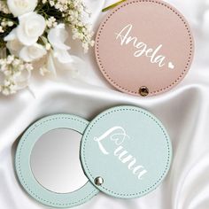 two personalized compact mirrors sitting on top of a white bed next to flowers and a bouquet