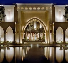 the entrance to a large building lit up at night with lights reflecting in the water