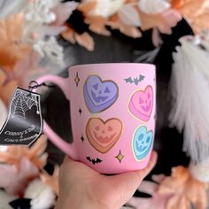 a hand holding a pink coffee mug with halloween stickers on it