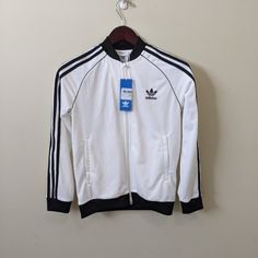 Addidas Junior Track Jacket M White/Black New With Tags. Zip Up Sporty White Track Jacket With Three Stripes, White Casual Track Jacket With Three Stripes, Casual White Track Jacket With Three Stripes, White Winter Track Jacket With Ribbed Cuffs, White Casual Track Jacket For Winter, White Casual Outerwear With Ribbed Cuffs, Casual White Outerwear With Ribbed Cuffs, Fitted White Outerwear With Ribbed Cuffs, White Winter Track Jacket For Streetwear