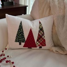 three christmas trees on a pillow sitting on a white couch next to a beaded ornament