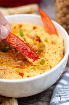 a person dipping something into a bowl of humongous food with carrots and green onions