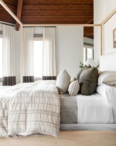 a bed with white linens and pillows in a bedroom next to two large windows