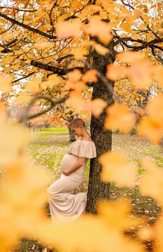 a pregnant woman leaning against a tree in the fall