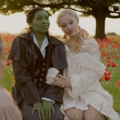 two people sitting in the grass with one person dressed as an elf and the other wearing a costume