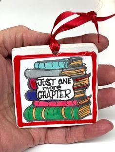 a hand holding a red and white ornament with books on it