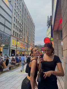 two women standing next to each other in front of buildings with neon signs on them