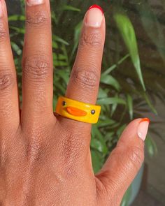 a woman's hand with an orange and yellow ring on her left thumb, in front of a potted plant