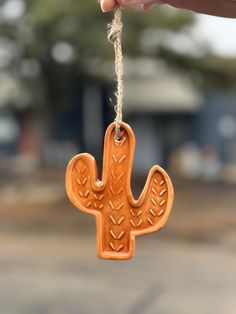 a wooden cactus ornament hanging from a string with a hand holding the string