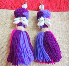 two purple and white tasselled earrings sitting on top of a table