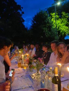 a group of people sitting at a long table with wine bottles and candles in front of them