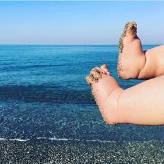 a person's feet covered in sand on the beach next to the ocean with blue sky and water