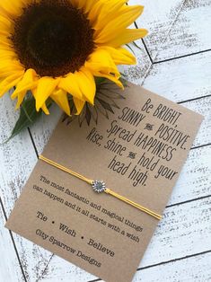 a yellow sunflower sitting on top of a card next to a paper with a message