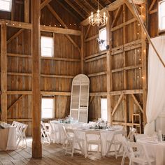 the inside of a barn with tables, chairs and chandeliers set up for an event