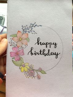 a person holding up a card with flowers on it that says happy birthday written in black ink